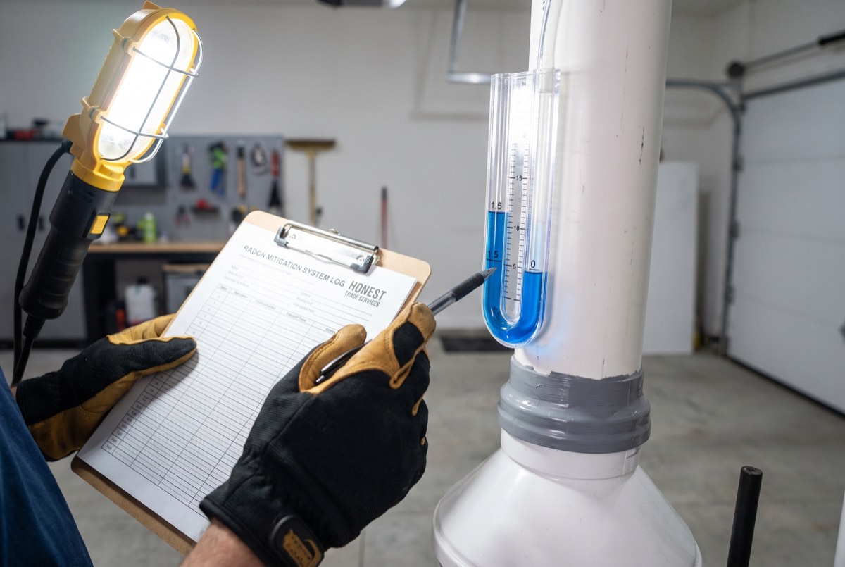 Technician checking the manometer gauge on a radon mitigation system pipe